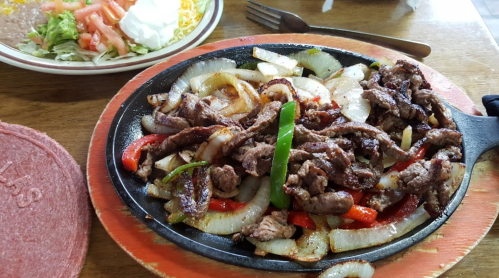 Sizzling beef fajitas with onions and peppers on a hot skillet, served with a side salad.