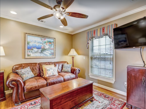 Cozy living room with a leather sofa, coffee table, lamp, and wall-mounted TV, featuring warm colors and decorative art.