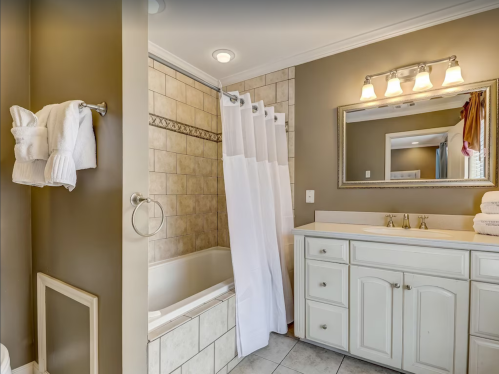 A modern bathroom featuring a bathtub, shower curtain, double sink vanity, and neatly arranged towels.