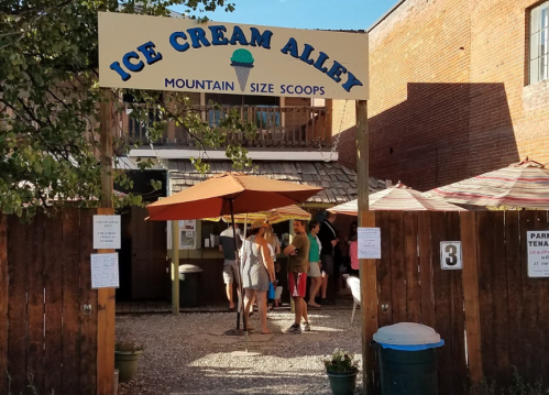 Entrance to Ice Cream Alley with a sign, outdoor seating, and people enjoying ice cream on a sunny day.