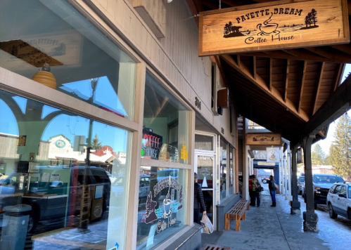Exterior of Payette Dream Coffee House, featuring a wooden sign and a sidewalk with benches and parked cars.