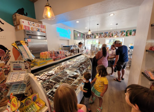 A busy ice cream shop with a display of treats, families enjoying their time, and colorful decor.
