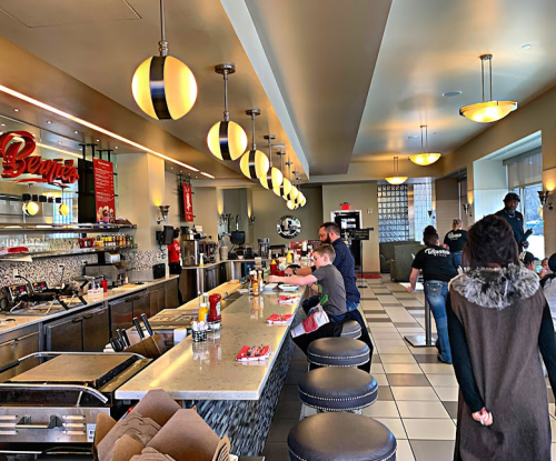 A modern diner interior with a long counter, patrons seated, and staff serving food under stylish pendant lights.