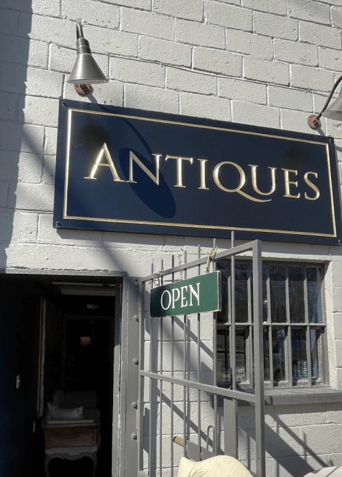 Sign for an antiques shop with "OPEN" displayed, set against a white brick wall.