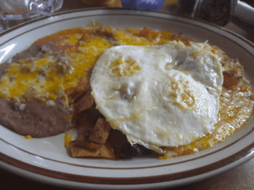 A plate of refried beans topped with cheese, alongside crispy tortilla pieces and a fried egg.