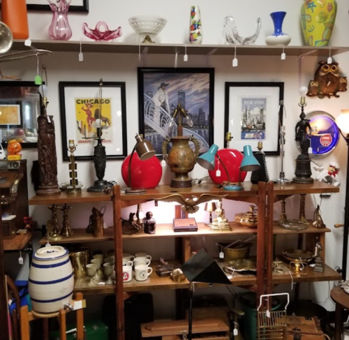 A display of various antiques, including lamps, vases, and framed art, arranged on wooden shelves.