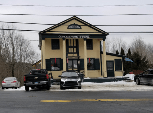 A historic building labeled "Colebrook Store," with parked cars in front and snow on the ground.