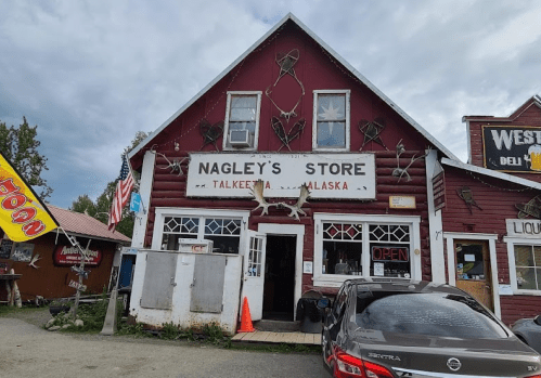 A rustic red building with a sign reading "Nagley's Store," featuring various outdoor decorations and an open sign.