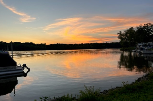 A serene sunset over a calm river, reflecting vibrant colors with boats docked along the shore.