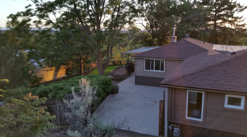 A view of a house with a sloped driveway, surrounded by trees and greenery, during sunset.