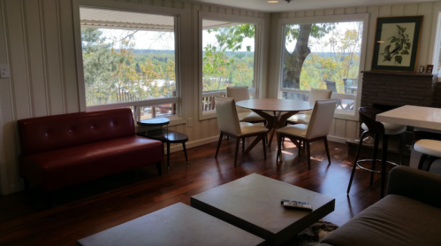 Cozy living space with a red sofa, dining table, and large windows showcasing a scenic outdoor view.