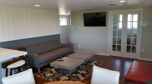 Modern living room with a gray sofa, coffee table, and a TV on the wall, featuring light walls and wooden flooring.