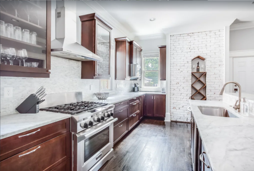 Modern kitchen with dark wood cabinets, marble countertops, stainless steel appliances, and a white brick accent wall.