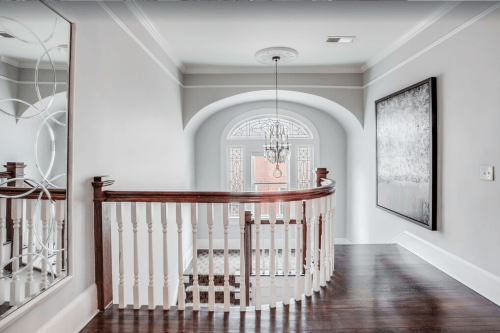 A spacious hallway with a curved staircase, chandelier, and large mirror, featuring elegant decor and natural light.