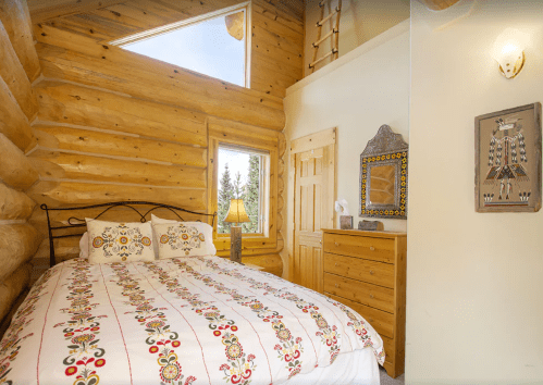 Cozy log cabin bedroom with a decorative bedspread, wooden walls, and a window letting in natural light.