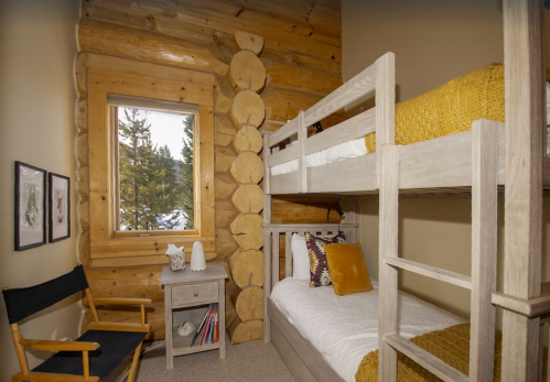Cozy log cabin bedroom with bunk beds, a chair, and a window showcasing a snowy landscape outside.