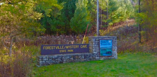 Sign for Forestville/Mystery Cave State Park, surrounded by trees and greenery.