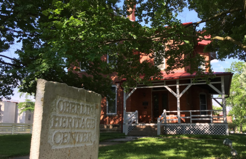 A brick building with a red roof, labeled "Gibert Heritage Center," surrounded by trees and greenery.