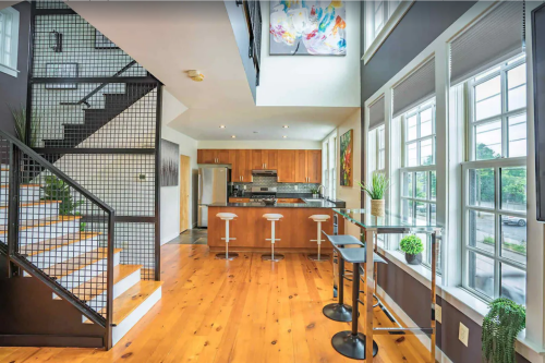 Modern open-concept kitchen and living area with wooden floors, large windows, and a stylish staircase.