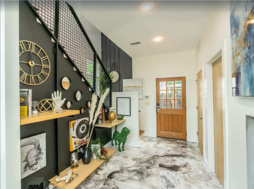 Modern entryway featuring a staircase, decorative shelves, wall art, and a wooden door with glass panels.