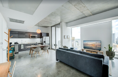 Modern apartment interior featuring a kitchen, living area with a sofa, and large windows with city views.