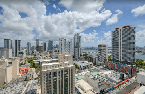 Aerial view of a vibrant city skyline with tall buildings, blue skies, and scattered clouds.