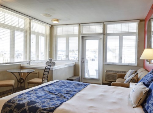 Cozy hotel room with a bed, seating area, and large windows offering a view of the outside. Bright and inviting decor.