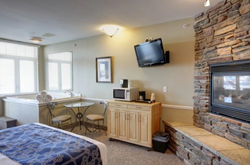 Cozy hotel room featuring a bed, kitchenette, dining table, and a stone fireplace with a TV mounted on the wall.