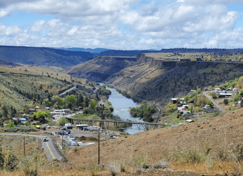 A scenic view of a river winding through green hills, with a small town and bridge visible in the foreground.