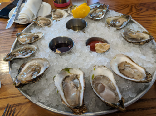 A platter of fresh oysters on ice, garnished with lemon and served with dipping sauces.