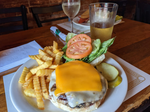 A plate with a cheeseburger topped with cheddar, fries, lettuce, tomato, and pickles, alongside a glass of beer and wine.