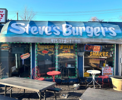 A colorful storefront of "Steve's Burgers" featuring a menu of burgers, chicken, fish, and shakes. Outdoor seating visible.