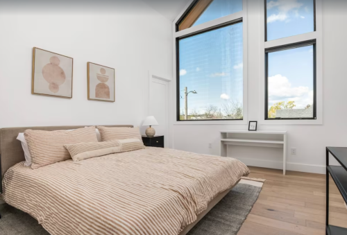 Bright bedroom with a striped bedspread, large windows, and minimalist decor featuring abstract art.