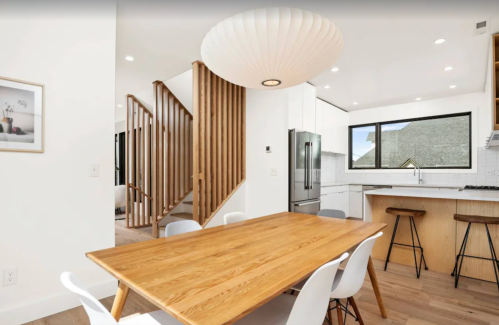 Modern kitchen and dining area with a wooden table, white chairs, and a staircase in a bright, open space.
