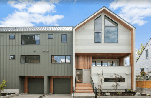 Modern two-story house with a mix of green and white siding, large windows, and a welcoming entrance.