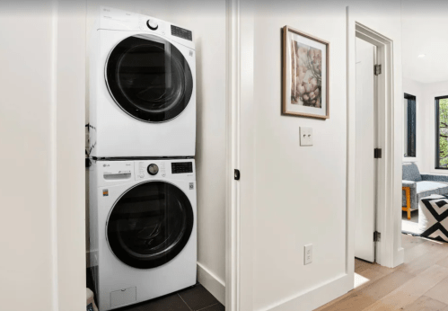 A stacked washer and dryer in a modern laundry nook with light walls and a framed picture nearby.