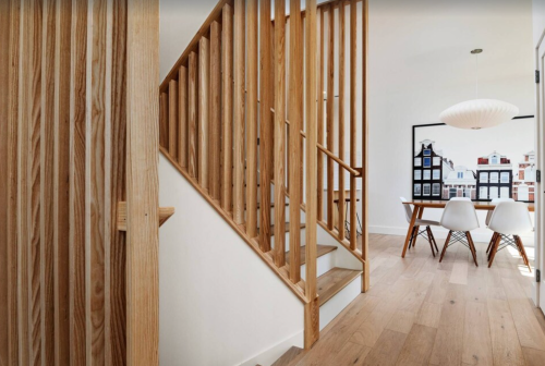 A modern interior featuring a wooden staircase and a dining area with a large artwork on the wall.