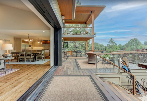 Modern outdoor deck with wooden flooring, overlooking a scenic view, connected to a stylish interior dining area.