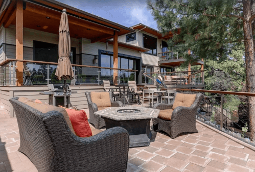 Outdoor patio with comfortable seating, a fire pit, and a view of a modern home surrounded by trees.