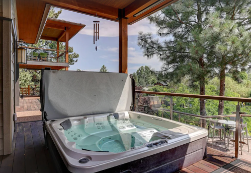 A hot tub on a wooden deck with a scenic view of trees and a distant building under a clear sky.