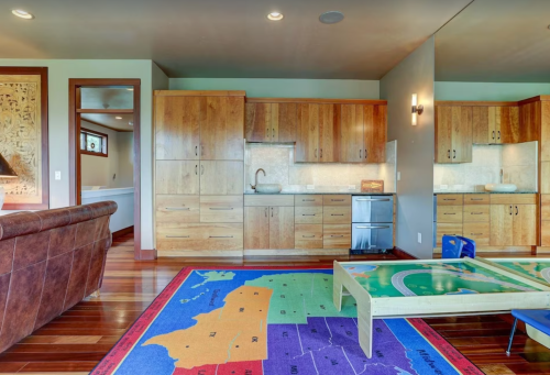 A modern kitchen with wooden cabinets, a small dining table, and a colorful map rug on the floor.
