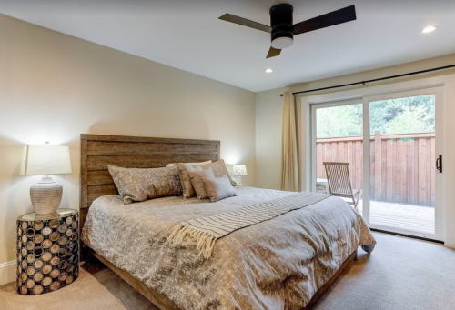 Cozy bedroom featuring a wooden bed, decorative pillows, a ceiling fan, and sliding doors to a patio.