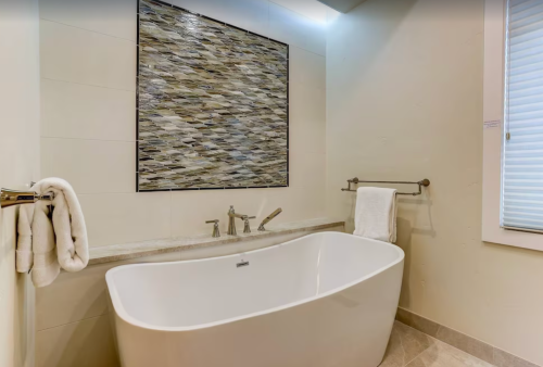 A modern bathroom featuring a freestanding tub, wall art, and a towel rack with neatly hung towels.