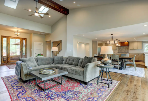 Spacious living area with a gray sectional sofa, wooden floors, and a dining area featuring a large table and modern decor.