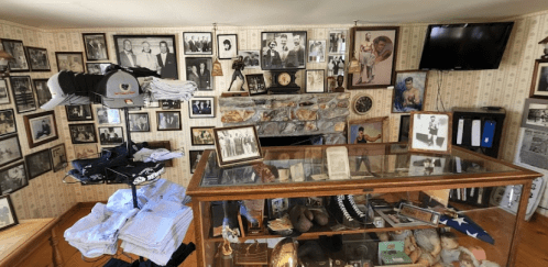 A room filled with vintage photographs, a display case, and memorabilia, featuring a stone fireplace and a TV.