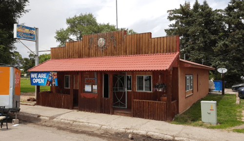 A rustic restaurant with a wooden facade and red roof, featuring an "Open" sign and outdoor seating.