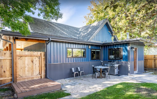 A blue and gray house with a wooden deck, outdoor seating, and a grill in a green yard.