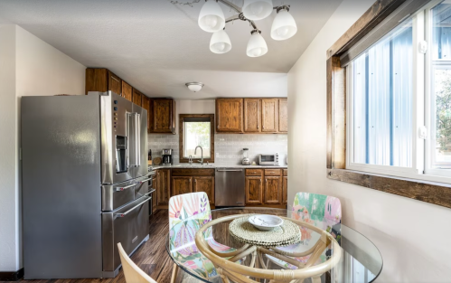 Bright kitchen with wooden cabinets, stainless steel appliances, and a round glass dining table with colorful chairs.