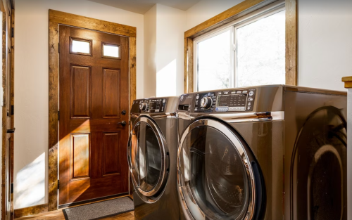 A laundry room featuring two black front-loading washing machines next to a wooden door and a window.