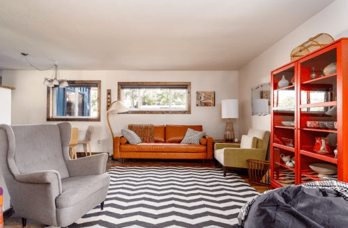 Cozy living room with a brown leather sofa, green chair, patterned rug, and colorful shelving unit. Bright and inviting space.